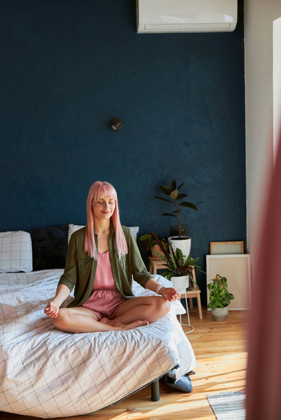 Peaceful woman in loose shirt and pajamas meditates in badroom - Foto, imagen