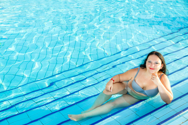 Smiling brunette woman lies in the pool. - Photo, image