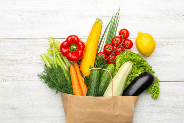 Vegetables in a paper bag on a white wooden background. Shopping in a supermarket or market. - Foto, immagini