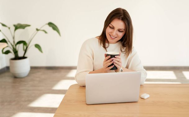 Lächelnde Frau mit Kaffee und Laptop am Arbeitsplatz - Foto, Bild