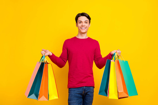 Photo of cool brunet millennial guy stand with bags wear red sweater isolated on yellow color background - Fotó, kép