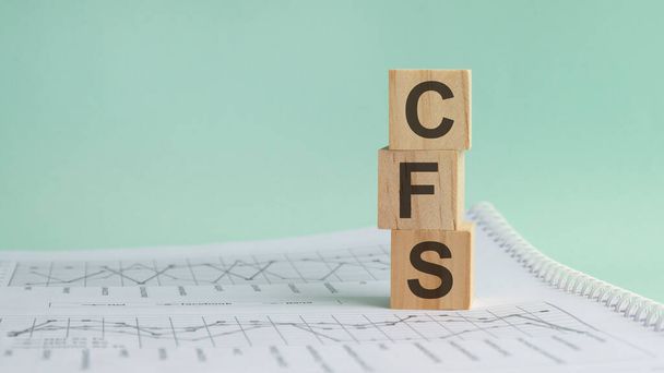 három kő kocka a fehér pénzügyi kimutatások hátterében, táblázatok a "CFS - acronim Consolidated Financial Statement" szóval. Erős üzleti koncepció. Szürke háttér. - Fotó, kép