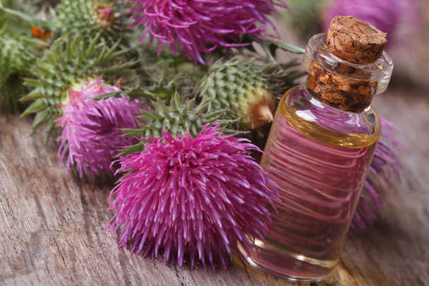 burdock oil in a glass bottle on a background of flowers - Photo, Image