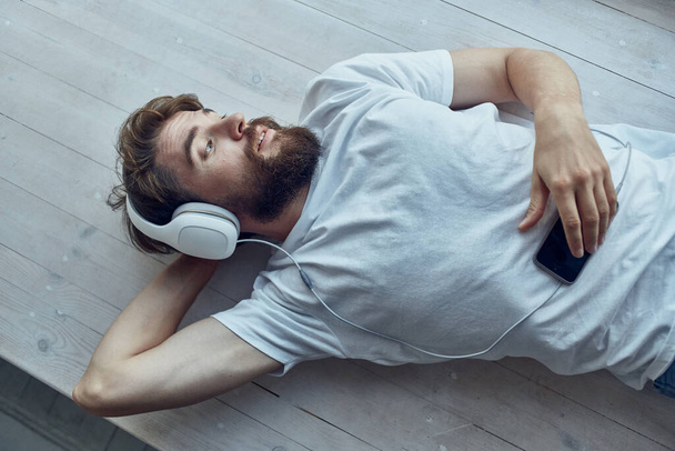 bearded man lying on the windowsill wearing headphones fun - Photo, Image