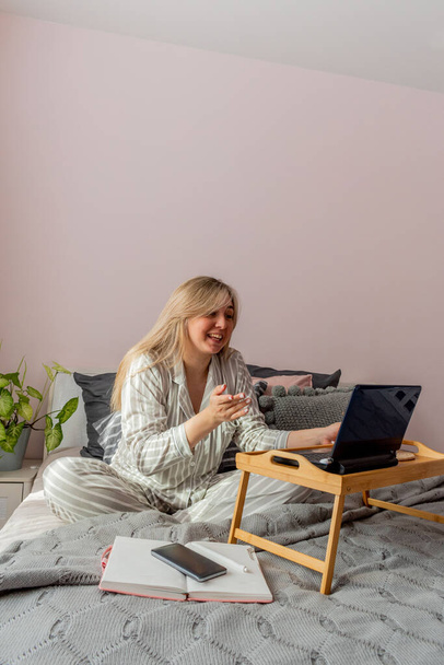 Defocus. Young woman in undergoing psychotherapy on Internet using a computer while sitting on bed in bedroom. Girl looks a laptop computer. People wellness concept. Comfort zone in the house. - 写真・画像