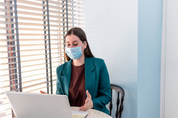 Young woman in suite with protective mask is working on computer. Businesswoman is keeping social distancing and working remotely. New normal concept - Φωτογραφία, εικόνα