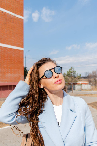 Young woman in mirrored sunglasses looks into the sky. Wellness concept. Adult girl walks and breathes fresh air in the spring. - Foto, Imagem