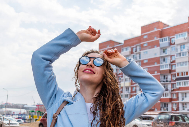 Young woman in mirrored sunglasses looks into the sky. Wellness concept. Adult girl walks and breathes fresh air in the spring. - Foto, afbeelding