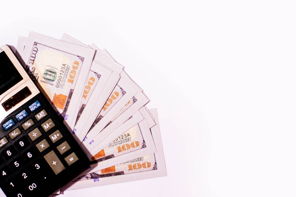 Contando papel moneda estadounidense cien dólares en una calculadora sobre fondo blanco aislado. - Foto, Imagen