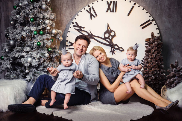A happy big family with twin children in the New Year's interior of the house against the background of a large clock. - Foto, Imagen