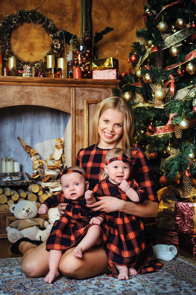 A happy mother with her twin children in the New Year's interior of the house on the background of a Christmas tree. - Foto, afbeelding