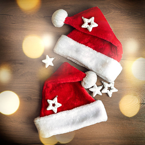 Concepto creativo mínimo de Navidad y Año Nuevo. Dos sombreros de Santa Claus borrosos sobre un fondo de madera con luces desenfocadas. Foto de alta calidad - Foto, imagen