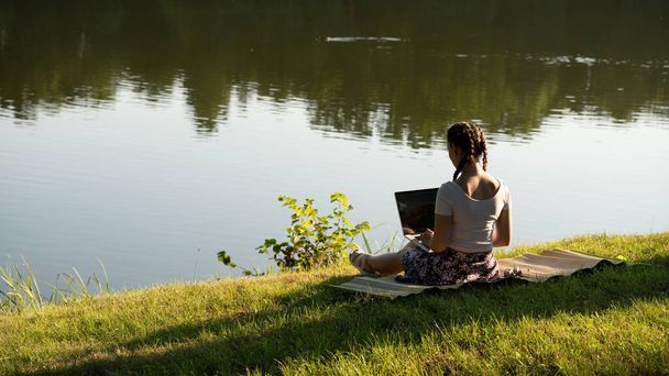 ラップトップ屋外ビジネス技術。学生の女の子は、夏の公園でタブレット、コンピュータ上で動作します。外の自然界のオンライン女性。幸せなヒップスター若い距離学習コンセプト - 写真・画像