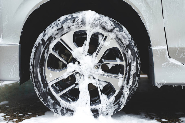 Car wash with active foam soap. cleaning wheel tire. commercial cleaning service concept. - Foto, imagen
