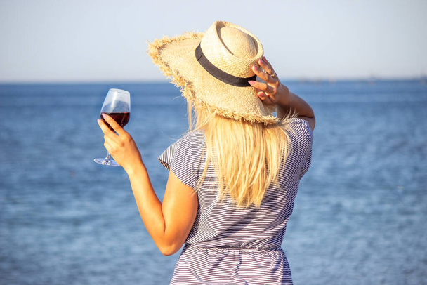 Beautiful smiling woman with a glass of wine on the beach. Fruit red wine. Selective focus. - Zdjęcie, obraz