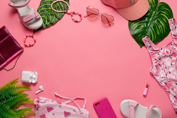 Beach fashion concept flat lay. Girls accessories and clothes with green leaves on pink background. Flat lay - 写真・画像