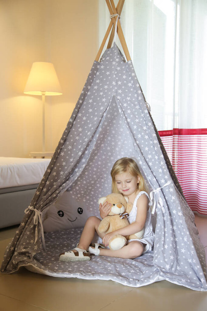 Cute toddler girl sitting in wigwam with her teddy bear in bedroom - Zdjęcie, obraz
