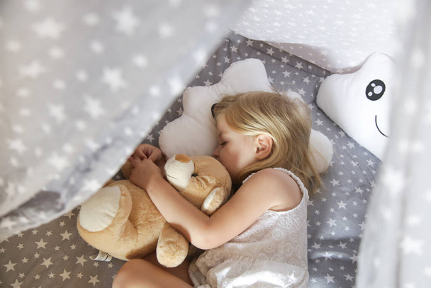 Linda niña durmiendo en sábanas con patrón de estrellas y almohada en forma de nube - Foto, imagen