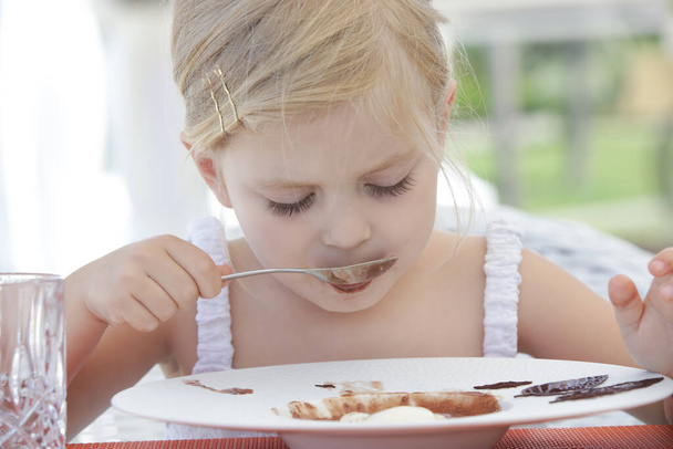 Cute toddler girl eating dessert in the outdoor restaurant - Foto, Imagem