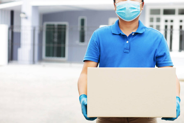 Een werknemer die een doos vasthoudt, levert producten aan klanten thuis. - Foto, afbeelding
