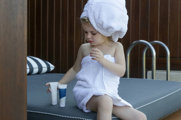 Skincare product for children. Little girl wrapped in towels using skin care products. - Photo, Image