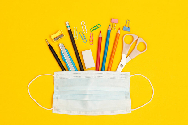 Concept of education top view mask and accessories stationery in the library at school yellow background - Photo, Image