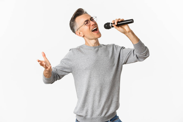 Portrait d'un homme passionné d'âge moyen chantant une sérénade au microphone, insouciant sur fond blanc - Photo, image