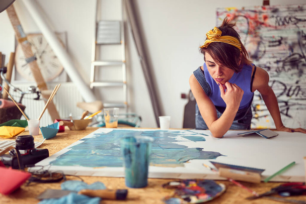 A young female artist brainstorming on a new painting she is working on in a pleasant atmosphere in the studio. Art, painting, studio - Photo, image