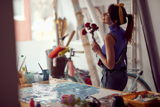 A young female artist is in a good mood while working on a new painting in a pleasant atmosphere in the studio. Art, painting, studio - Фото, зображення