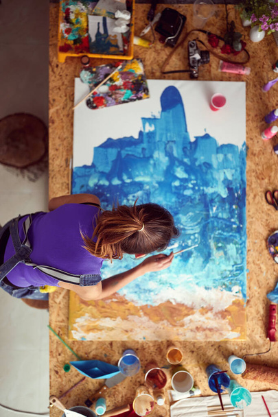 A bird's-eye view of a young female artist who is working on the painting in a creative atmosphere in her studio. Art, painting, studio - Foto, afbeelding