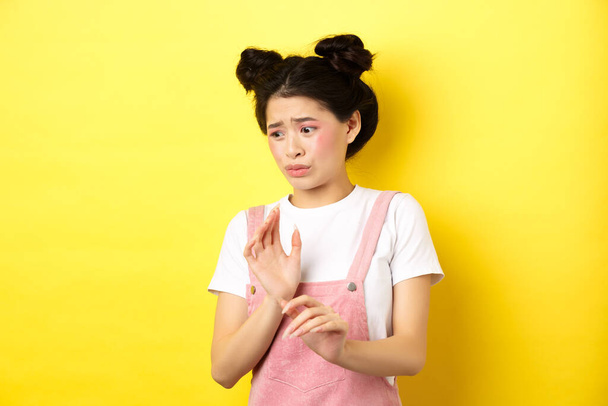 Отвратительная азиатка, поднимающая руки, защищающаяся, блокирующая что-то отвратительное, отворачивающаяся от отвращения и нежелания, стоящая на жёлтом фоне - Фото, изображение