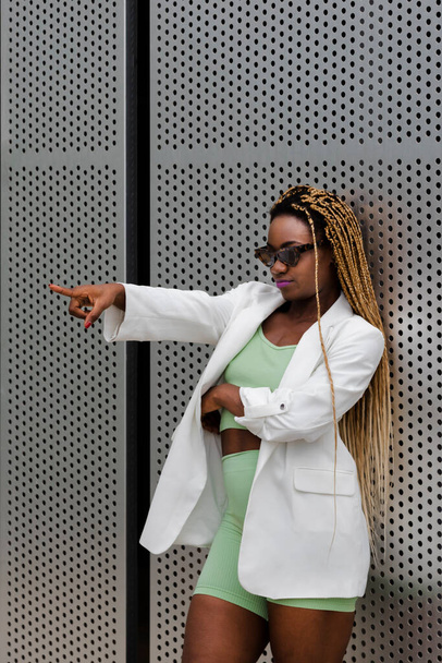 Young african american woman with long braids wearing sunglasses pointing index finger at someone. Vertical image. - Fotó, kép