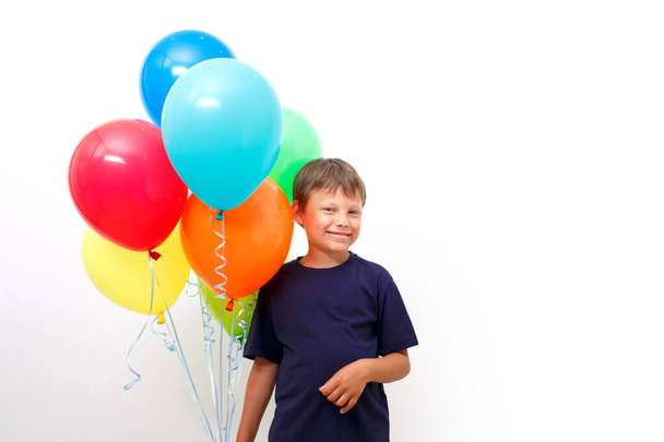 Happy eight year old boy with an armful of bright colorfull balloons celebrates birthday. light background. Copy space. - Photo, image