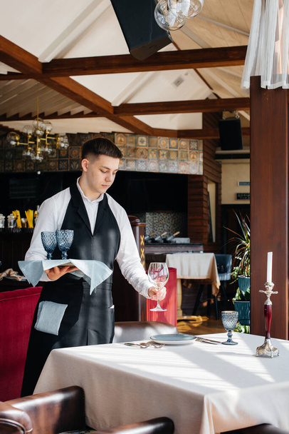 A young male waiter in a stylish uniform is engaged in serving the table in a beautiful gourmet restaurant. Restaurant activity, of the highest level. - Foto, Bild