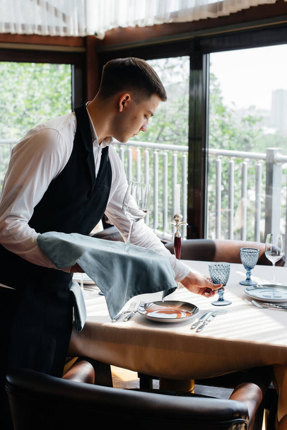 A young male waiter in a stylish uniform is engaged in serving the table in a beautiful gourmet restaurant. Restaurant activity, of the highest level. - Fotó, kép