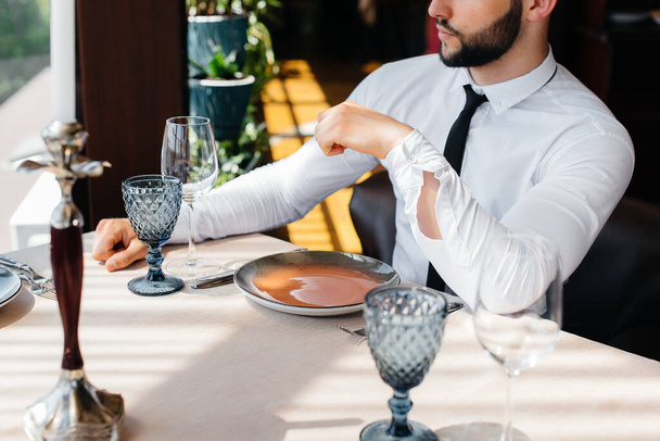A young bearded male businessman is sitting at a table in a fine restaurant and waiting for his order. Customer service in the catering. - Foto, afbeelding