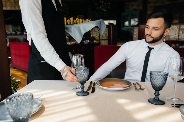 A stylish waiter serves a young couple who came on a date in a gourmet restaurant. Customer service in the catering. - Photo, Image