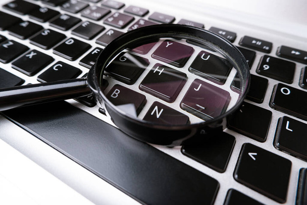Magnifying glass, loupe laying on a laptop keyboard. Technology file search tool concept, data forensics, computer crime and device investigation, closeup - Photo, Image