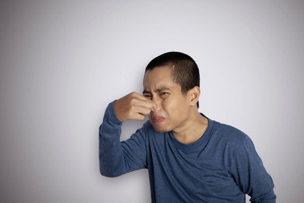 Portrait de jeune homme pincant le nez sur son visage en raison d'une mauvaise odeur isolée sur fond gris - Photo, image