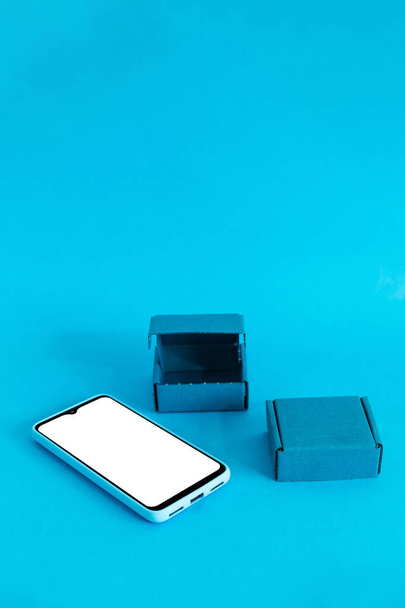 A vertical shot of a smartphone and two boxes isolated on a blue background - Fotografie, Obrázek