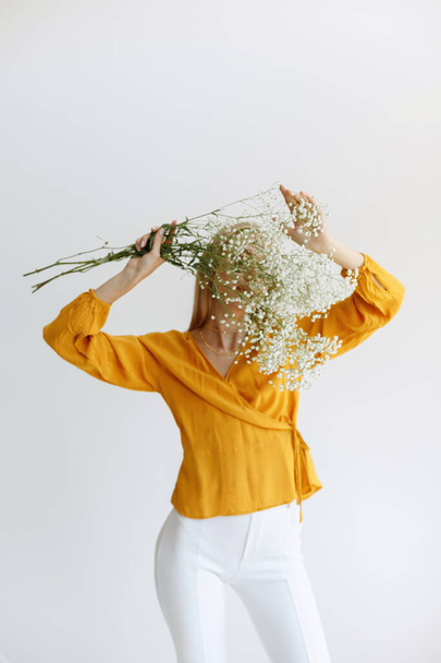 blondynka zakrywa twarz suchymi białymi kwiatami. romantyzm. bloger, wczesna jesień - Zdjęcie, obraz