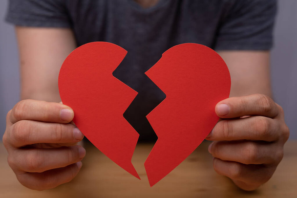 A closeup of a man holding a paper cutout of a broken heart - heartbreak concept - Zdjęcie, obraz