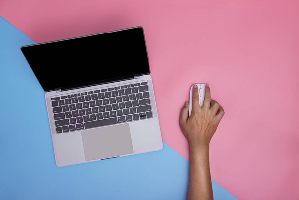 Man met laptop en draadloze muis op roze en blauwe achtergrond. kopieer ruimte. bovenaanzicht. - Foto, afbeelding