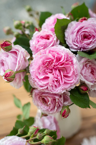 A vertical shot of a bouquet of pink garden roses in a vase on the table with a blurry background - 写真・画像