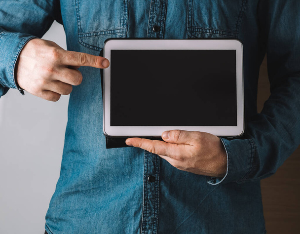 A closeup shot of a male holding and pointing to a tablet with a blank screen - Photo, image