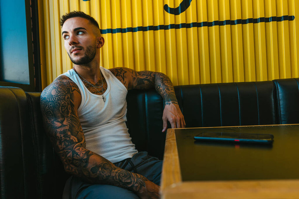 A handsome tattooed male sitting in the cafe and looking around - Fotó, kép