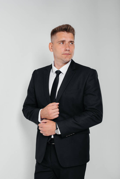 A handsome young man in a stylish black suit poses on a white background. A stylish business man. A big businessman. - Фото, изображение