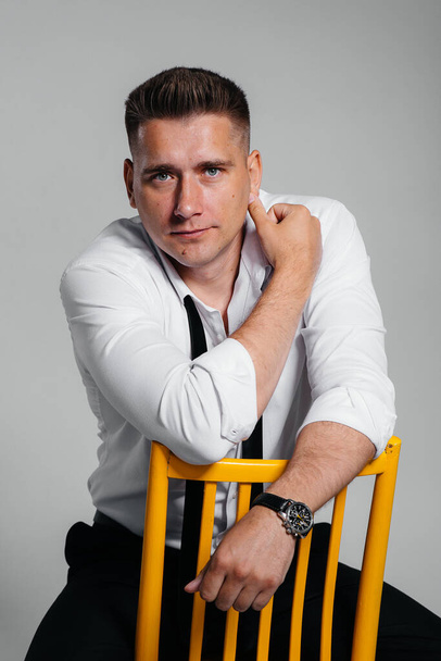 A stylish young man in a white shirt is sitting on the director's chair on a black background. A handsome charismatic businessman. - Foto, Imagen