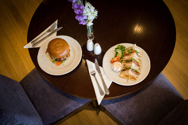 A top view of a delicious hamburger and a club sandwich served on a table for two in a restaurant - Foto, Bild