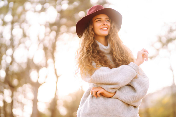 Young woman in sweater and hat enjoys a Autumn day outdoors in a park. Fashion, style concept. - Fotoğraf, Görsel